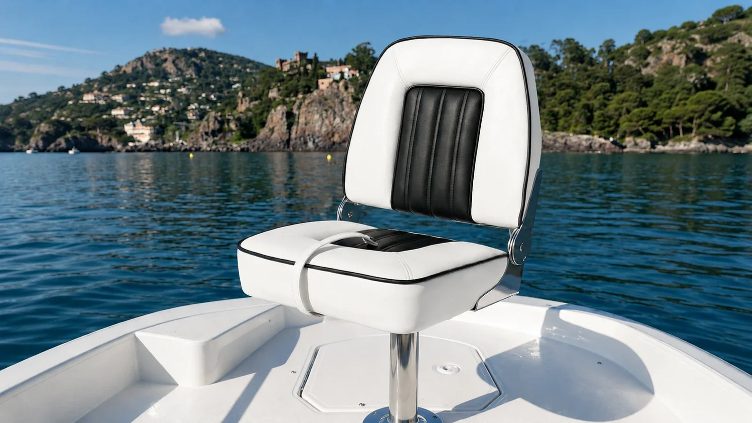 White and black folding boat seat mounted on a pedestal with calm blue water and a rocky coastline in the background.