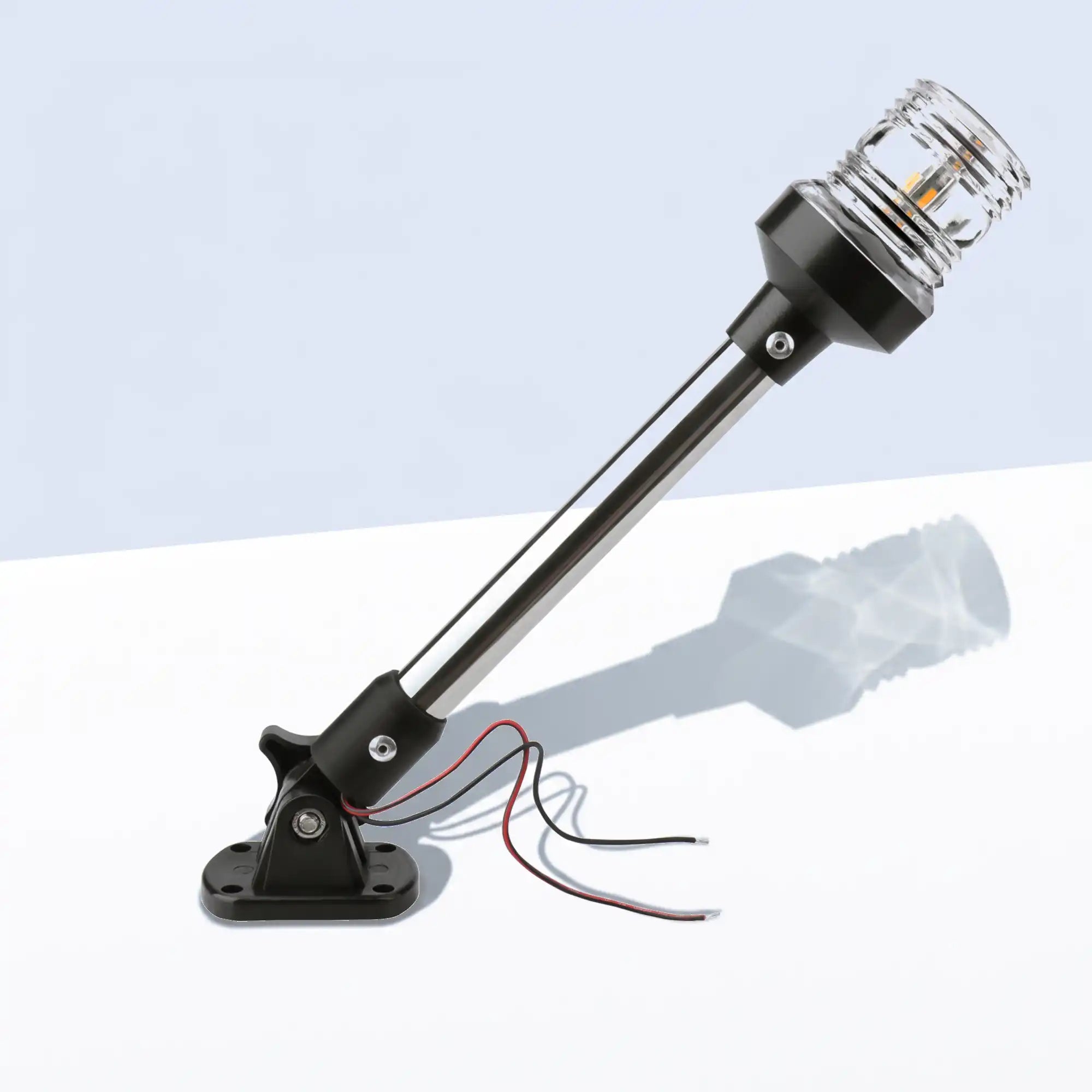Marinexplore 12-inch black anchor light with an extended pole and clear ribbed lens glowing warm white, mounted on a folding black base with red and black wire leads, photographed at an angle on a light gray studio backdrop.