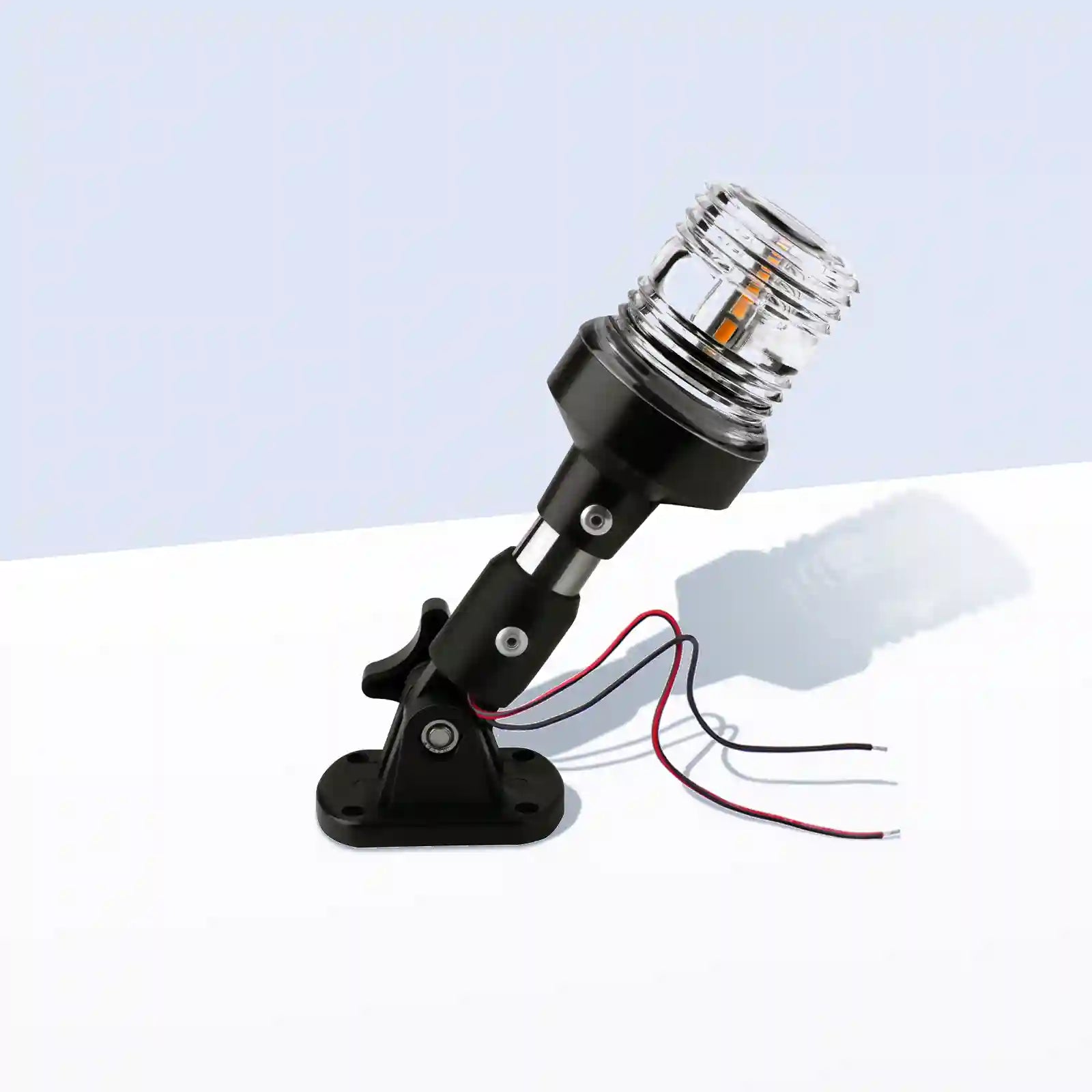 Marinexplore 6-inch black stainless steel boat anchor light with a clear ribbed lens glowing warm white, mounted on a folding black base with red and black wire leads, photographed at an angle on a light gray studio backdrop.