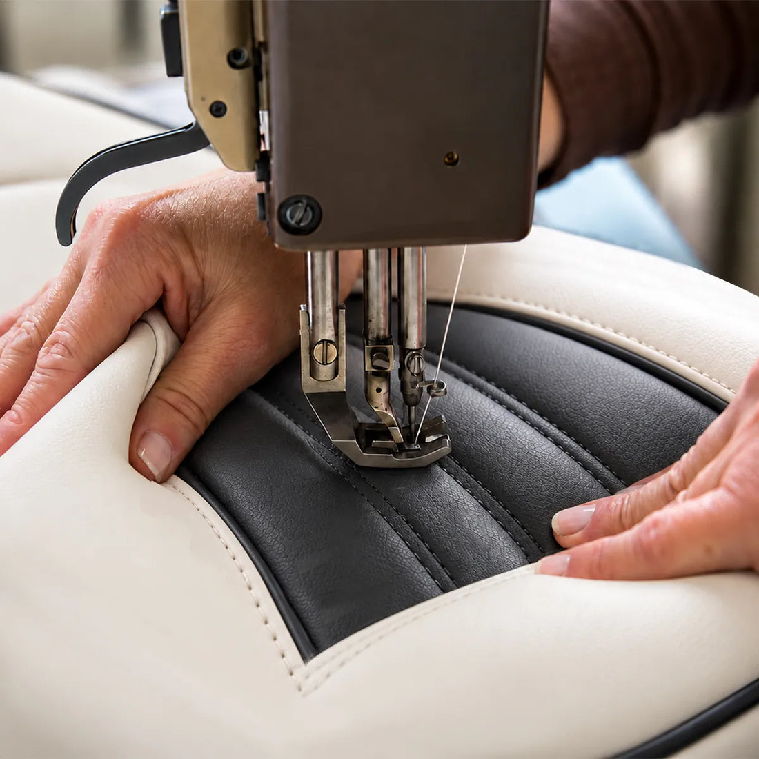 Close-up of an industrial sewing machine stitching black and white boat seat upholstery.