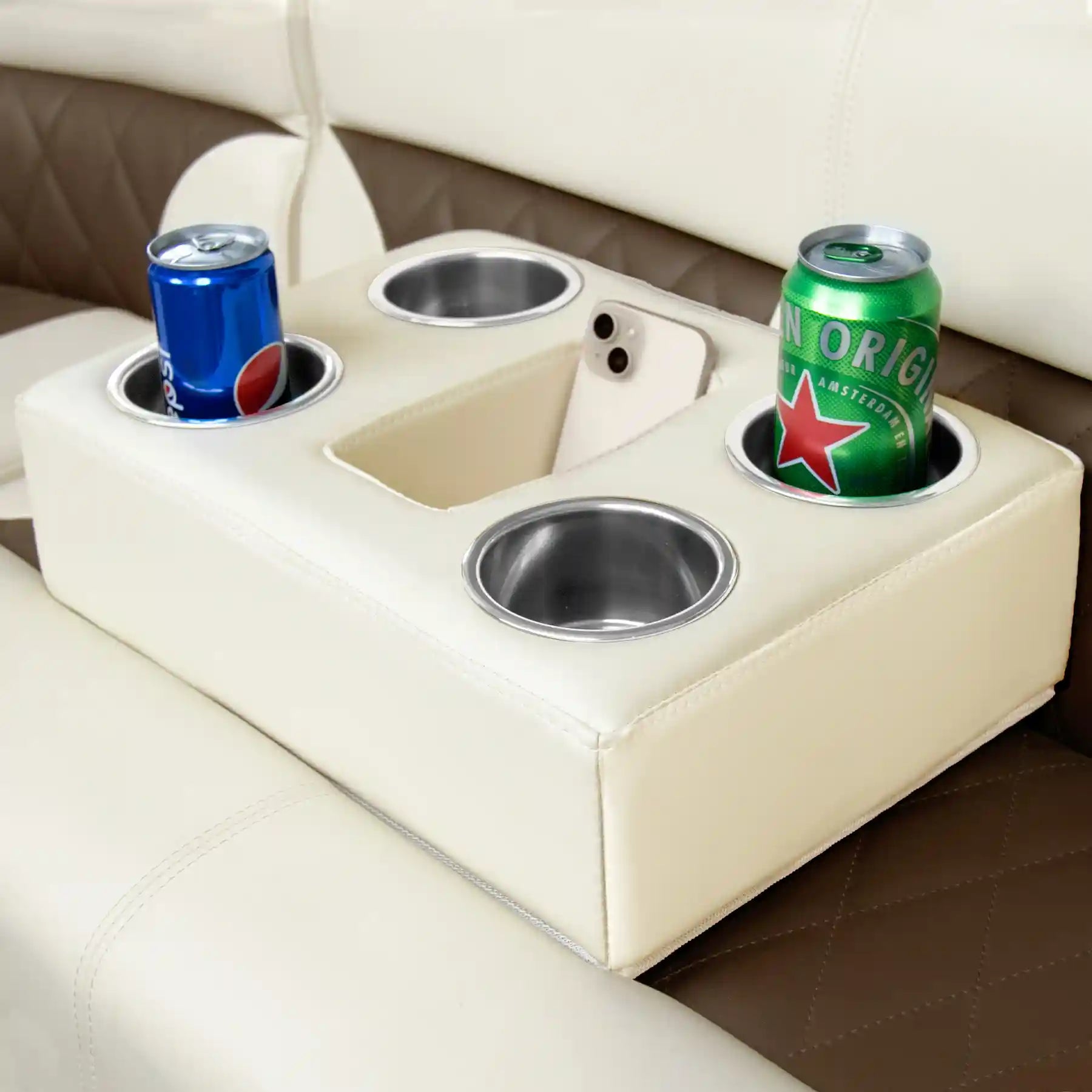 Marinexplore beige pontoon boat cup holder wedged between brown and white quilted leather boat seats, with a blue Pepsi can on the left, a green Heineken can on the right, a white phone in the center storage slot, and one empty stainless steel cup insert visible in front.