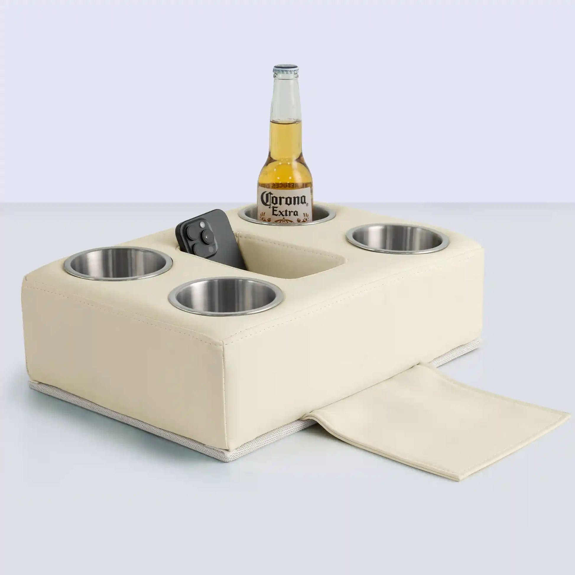Marinexplore beige PU leather pontoon cup holder with four stainless steel cup inserts, a center storage slot holding a black smartphone, a Corona beer bottle in one cup, and the bottom anchor strap pulled out, photographed from a front angle on a light gray surface.
