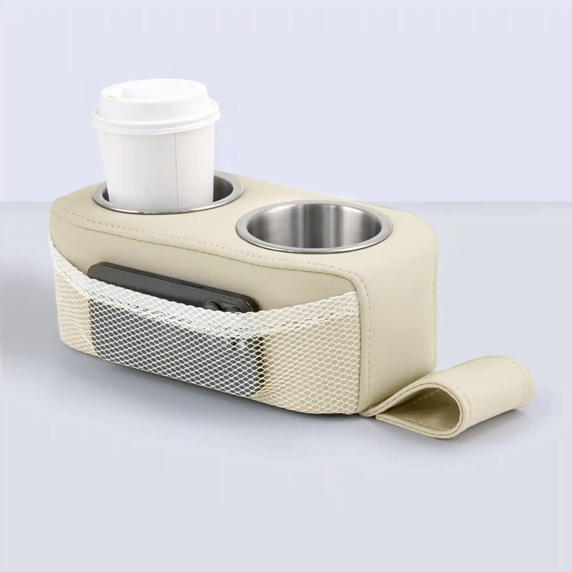 Marinexplore beige PU leather pontoon cup holder with dual stainless steel cup inserts, a white lidded coffee cup held securely in the left slot, a black phone tucked into the white mesh side pocket, and the beige fabric anchor strap extended flat in front on a gray surface.