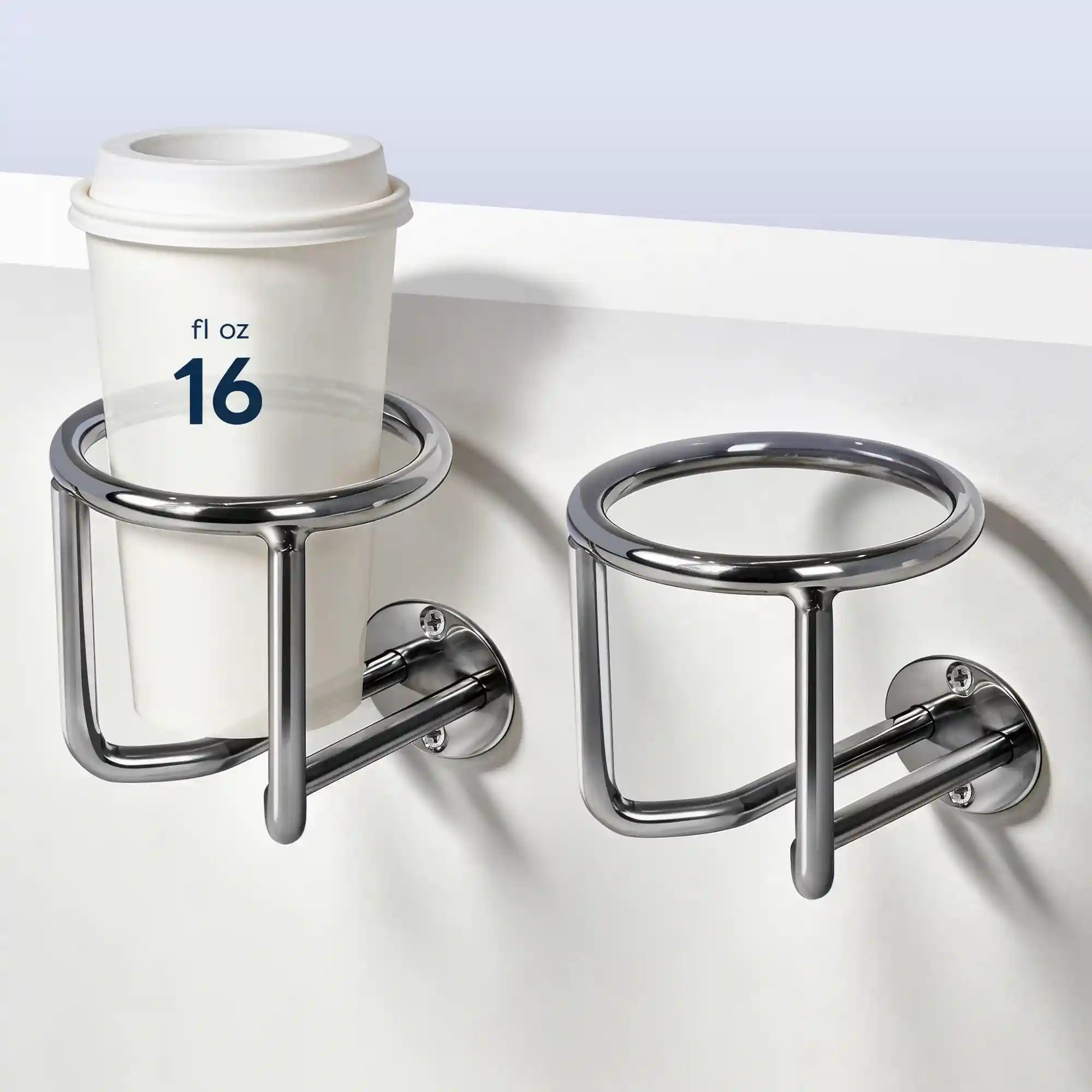 Two Marinexplore chrome stainless steel boat cup holders mounted side by side on a white surface edge, with a 16 fl oz white lidded coffee cup secured in the left holder and the right holder shown empty, photographed from a front diagonal angle against a light gray background.